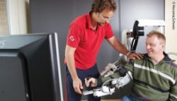 Foto: Ein Physiotherapeut trainiert mit seinem Patienten am ArmeoPower; Copyright: Hocoma, Schweiz